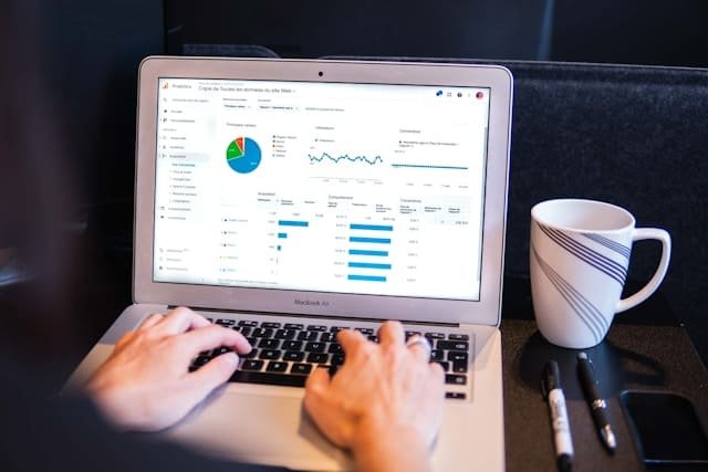 Notebook moderno exibindo um painel de vendas e gráficos de um e-commerce integrado, posicionado ao lado de uma caneca e canetas.